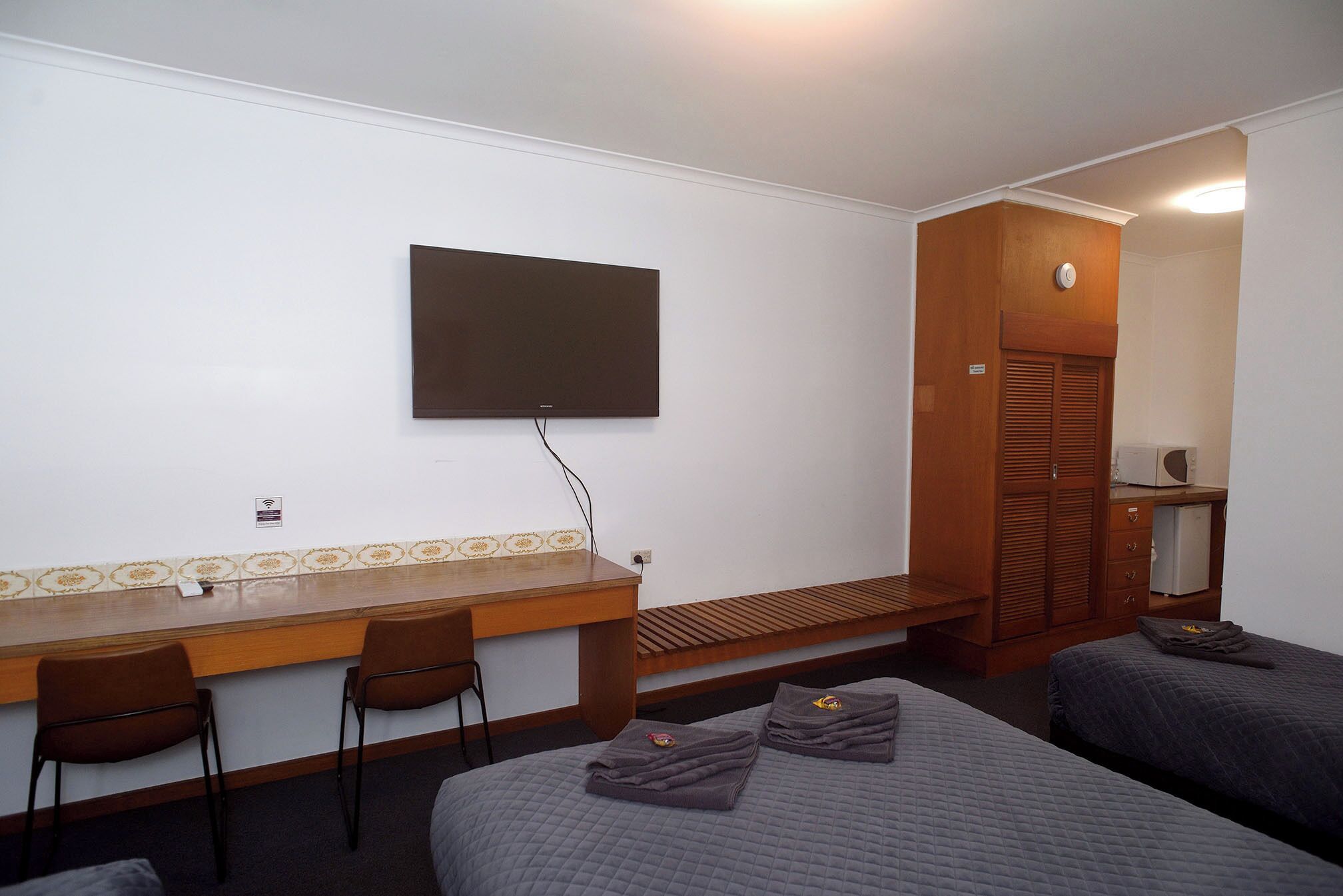 A hotel room with a bed, a desk with chairs, a television, and a wardrobe.