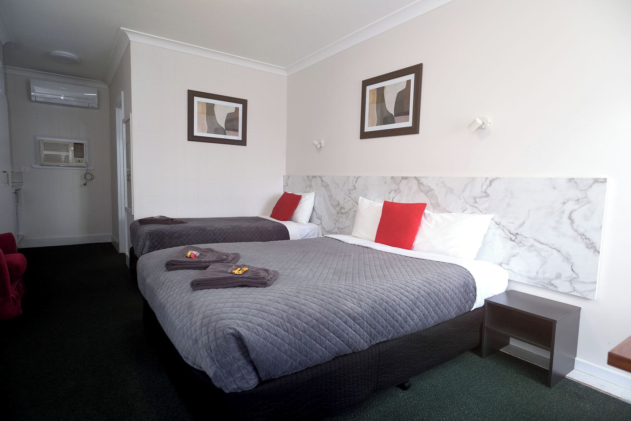 Une chambre d’hôtel avec deux lits, une tête de lit en marbre et des œuvres d’art accrochées aux murs.