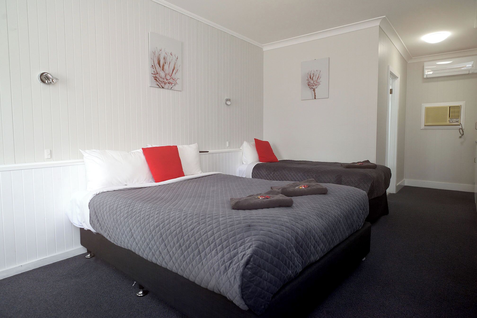 A hotel room with two beds, white paneled walls, and artwork.