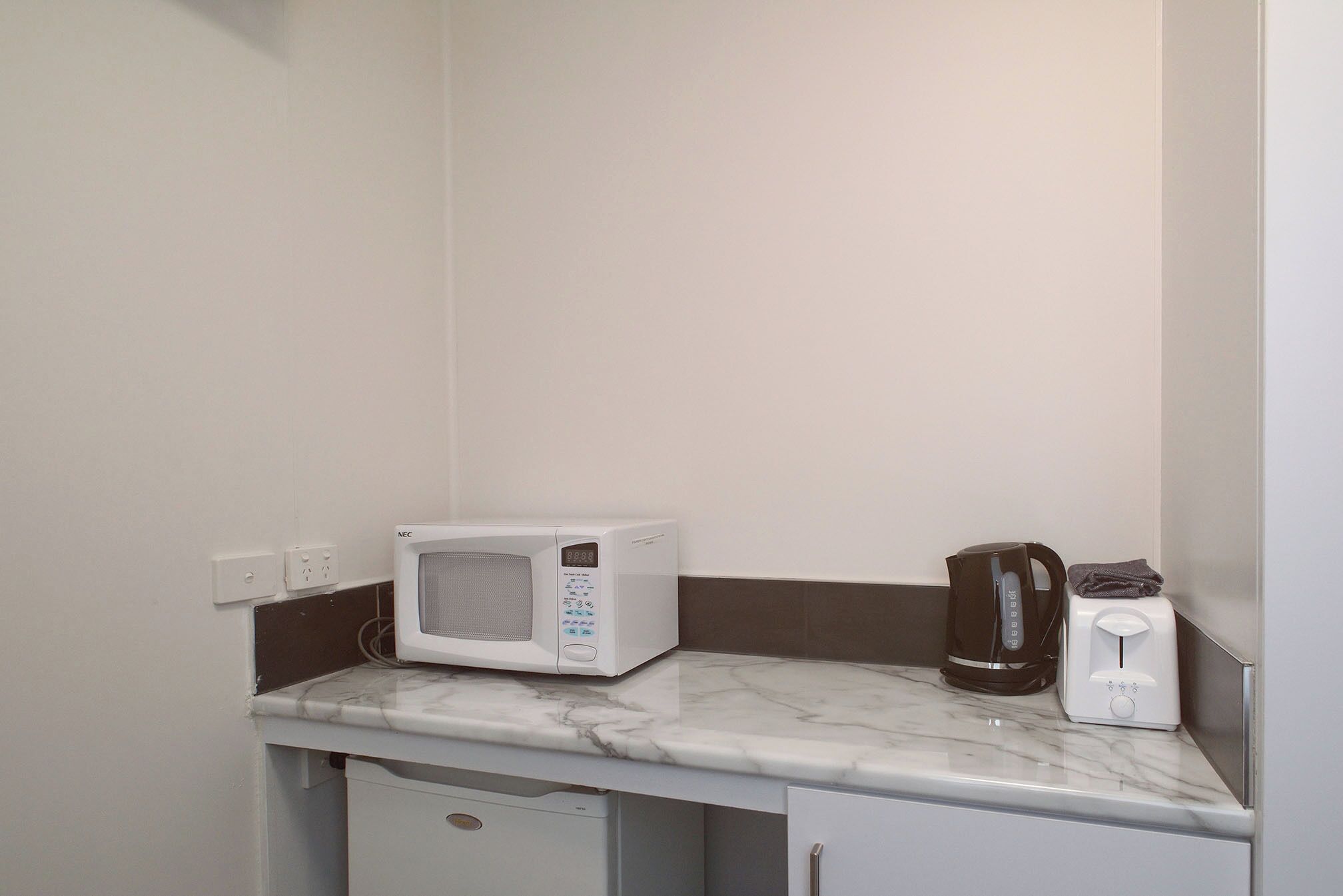 A kitchen with a microwave, coffee maker, and toaster on a marble countertop.