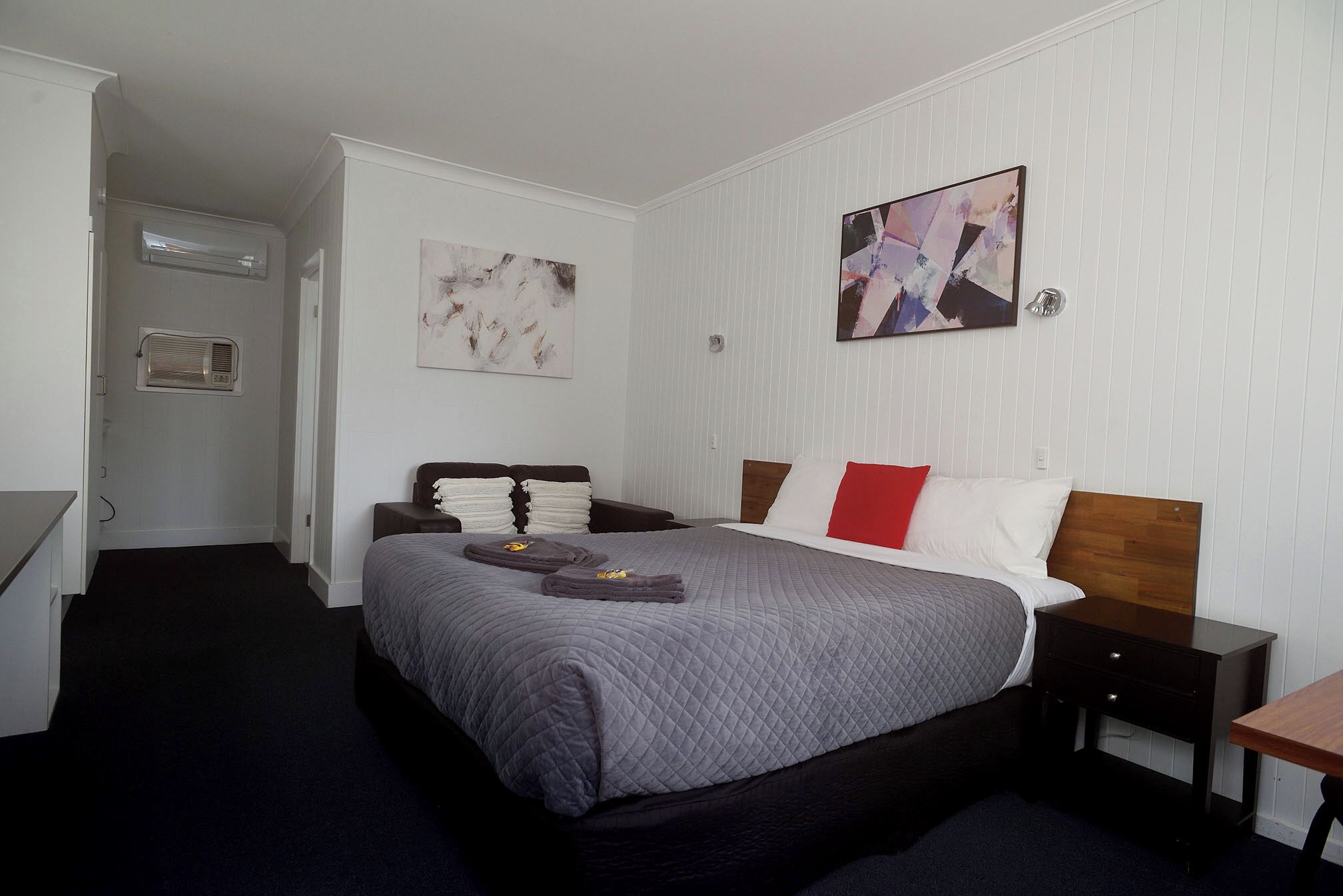 Una camera d'albergo con un letto, un comodino, una scrivania e un condizionatore d'aria a parete.