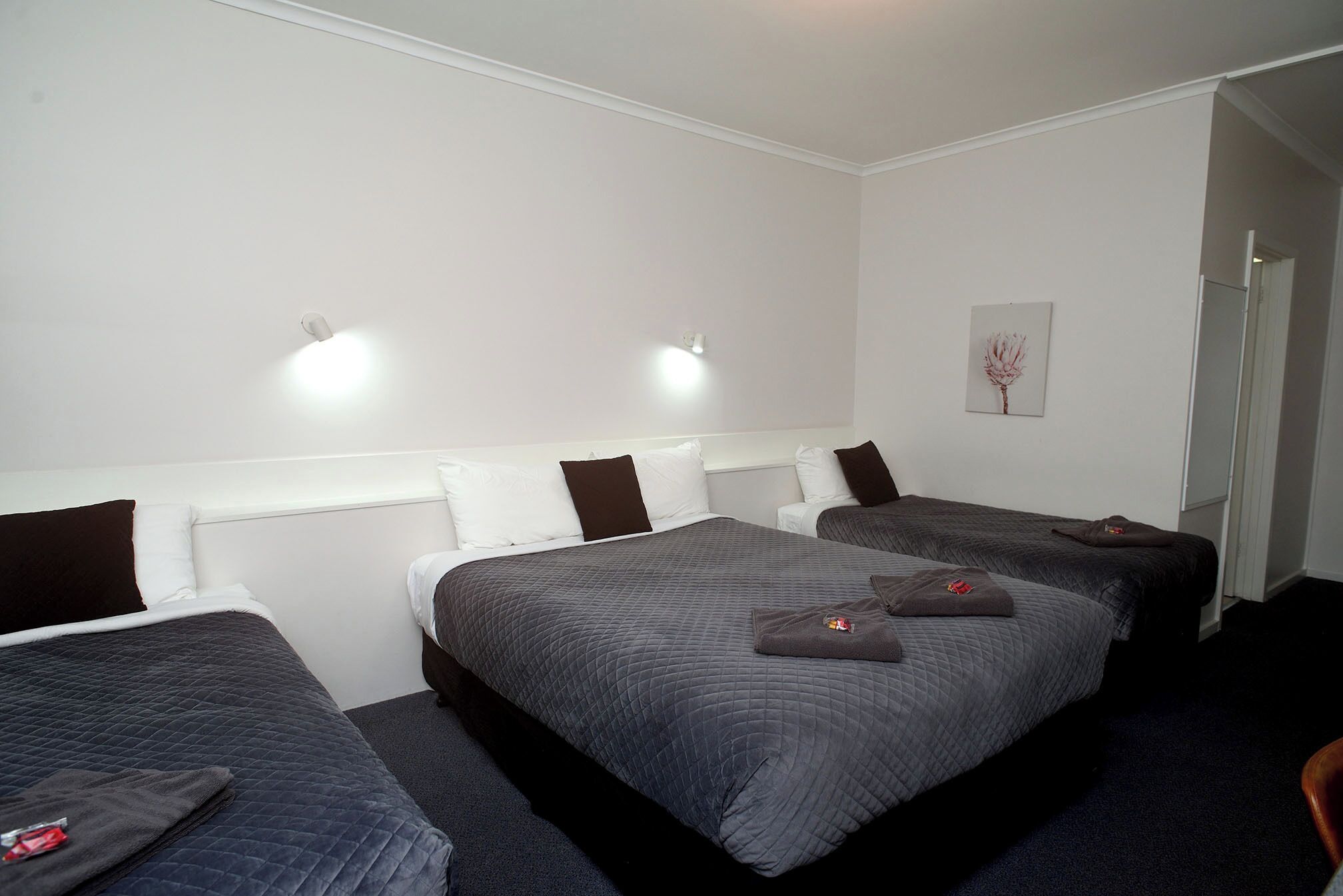 A hotel room with three beds, white walls, and a framed picture on the wall.