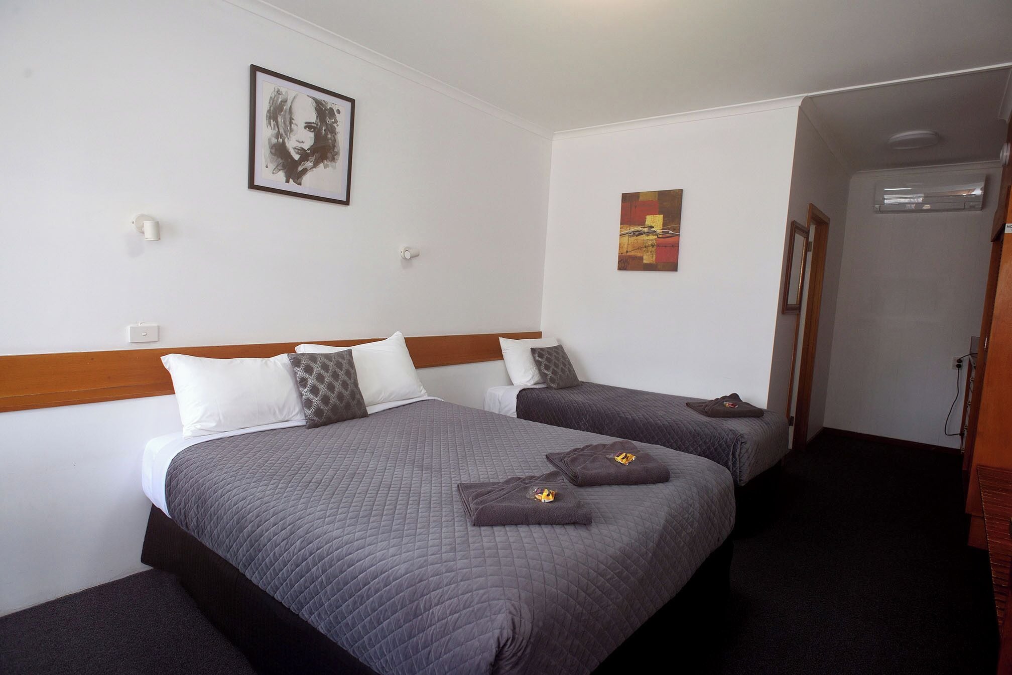 A hotel room with two beds, a framed picture on the wall, and a door leading to another room.