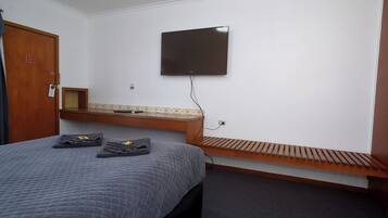 Quarto de hotel com uma cama, uma TV de tela plana na parede, um banco de madeira e uma pequena mesa de madeira.
