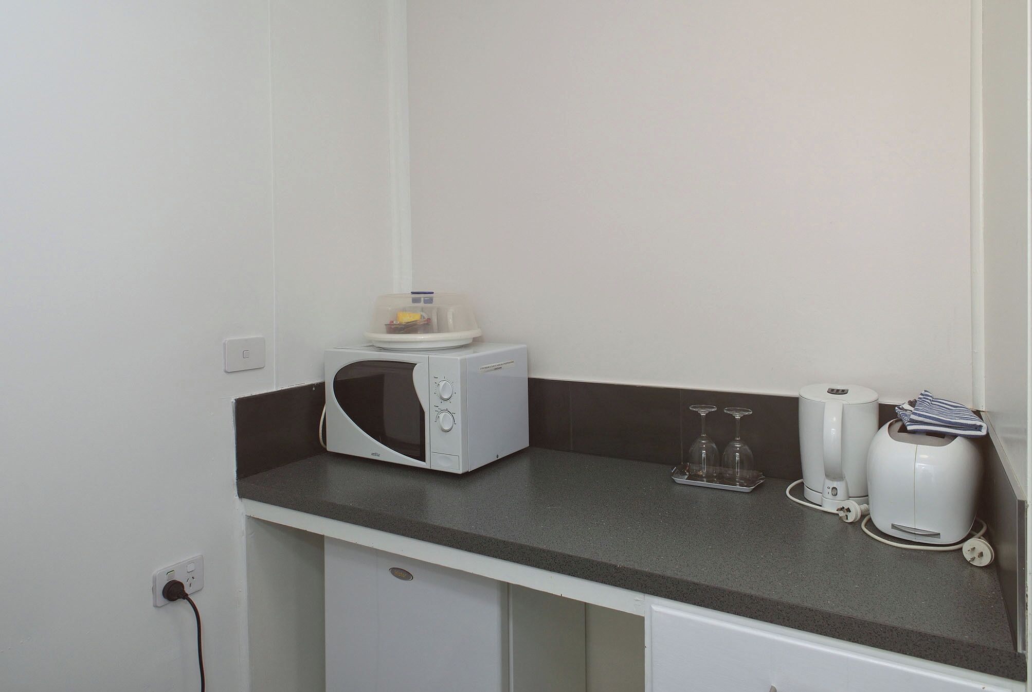 Una kitchenette equipada con microondas, cafetera y un pequeño armario.