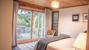 Ein Schlafzimmer mit einem großen Bett, einem Sessel, einem Fenster mit Vorhängen und Blick ins Freie.