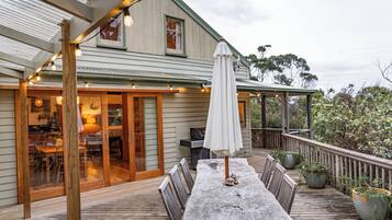 A wooden deck with a table and chairs, a barbecue grill, and a covered patio area.