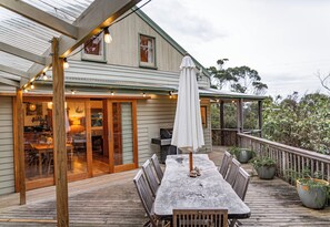 A wooden deck with a table and chairs, a barbecue grill, and a covered patio area.