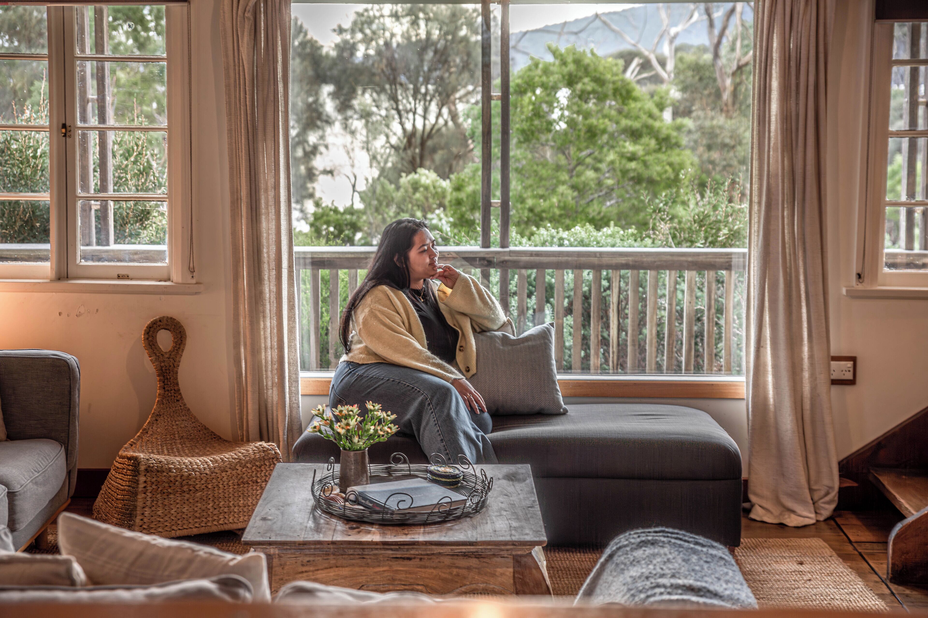 A cozy room with a large window, a sofa, a wicker chair, and a small table with a vase of flowers.