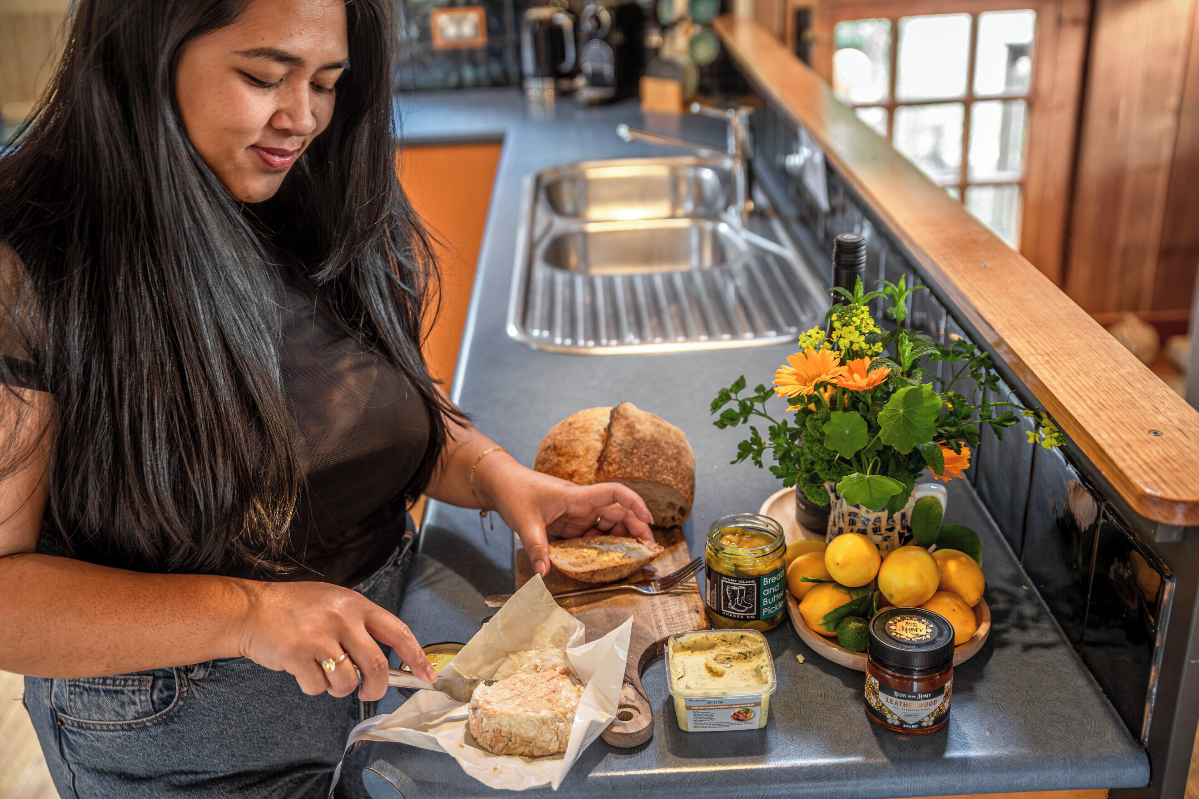 A person preparing food at a kitchen counter with bread, a jar of honey, and a bowl of lemons.