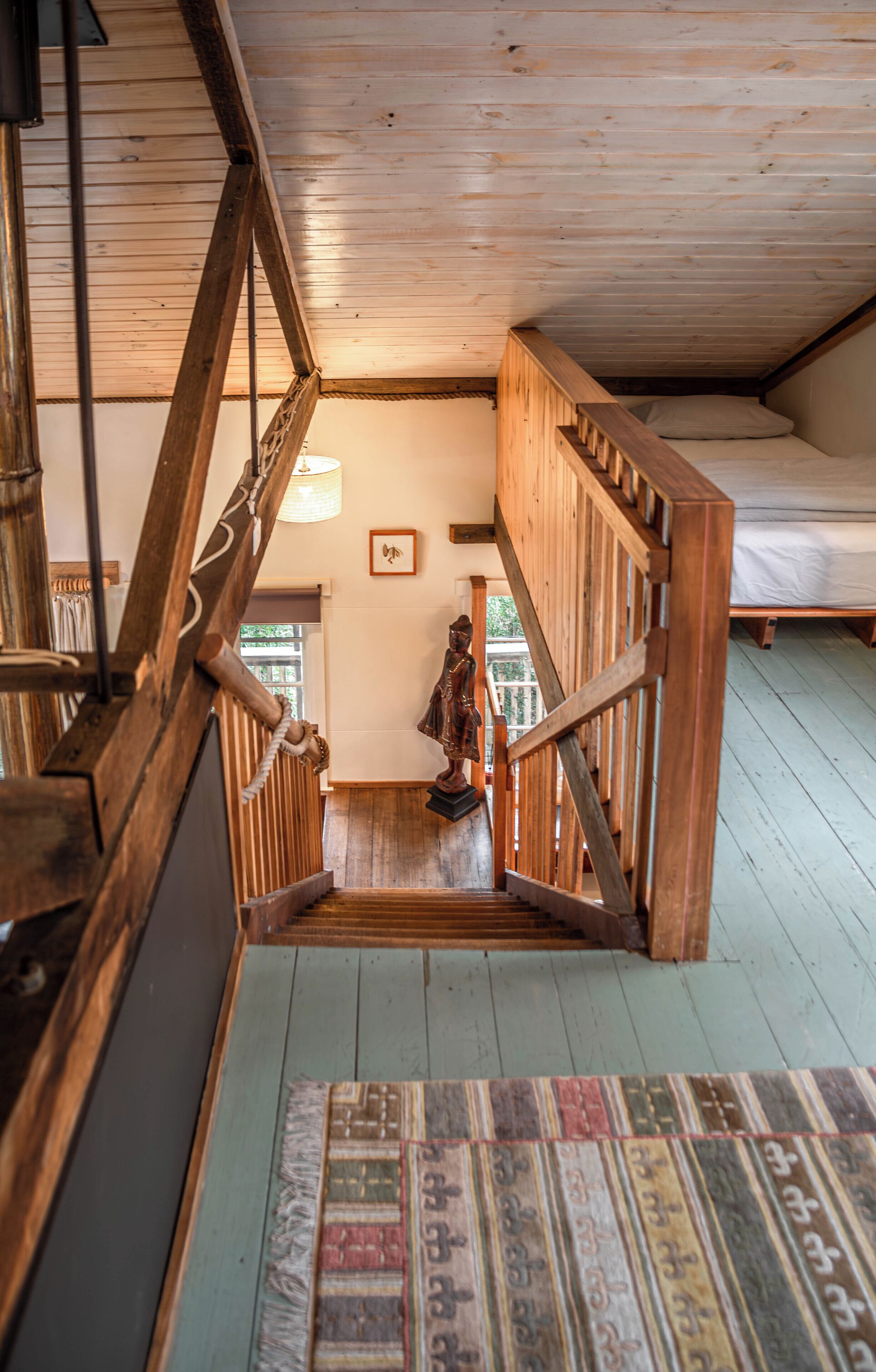 A wooden staircase leading to a bedroom with a bed and a window.