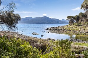 A natural landscape with a lake, rocky shore, and distant mountains. - Mandala Bruny Island (Alonnah)