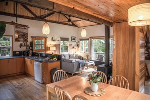 A spacious kitchen with wooden cabinets, a dining area with a table and chairs, and a cozy living room with a sofa and a fireplace. - Mandala Bruny Island (Alonnah)