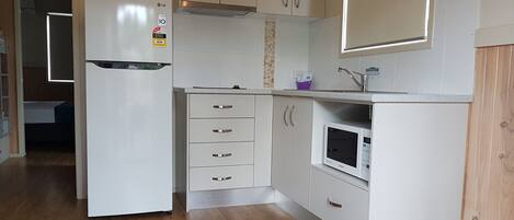 A compact kitchen with white cabinets, a built-in microwave, and a refrigerator.