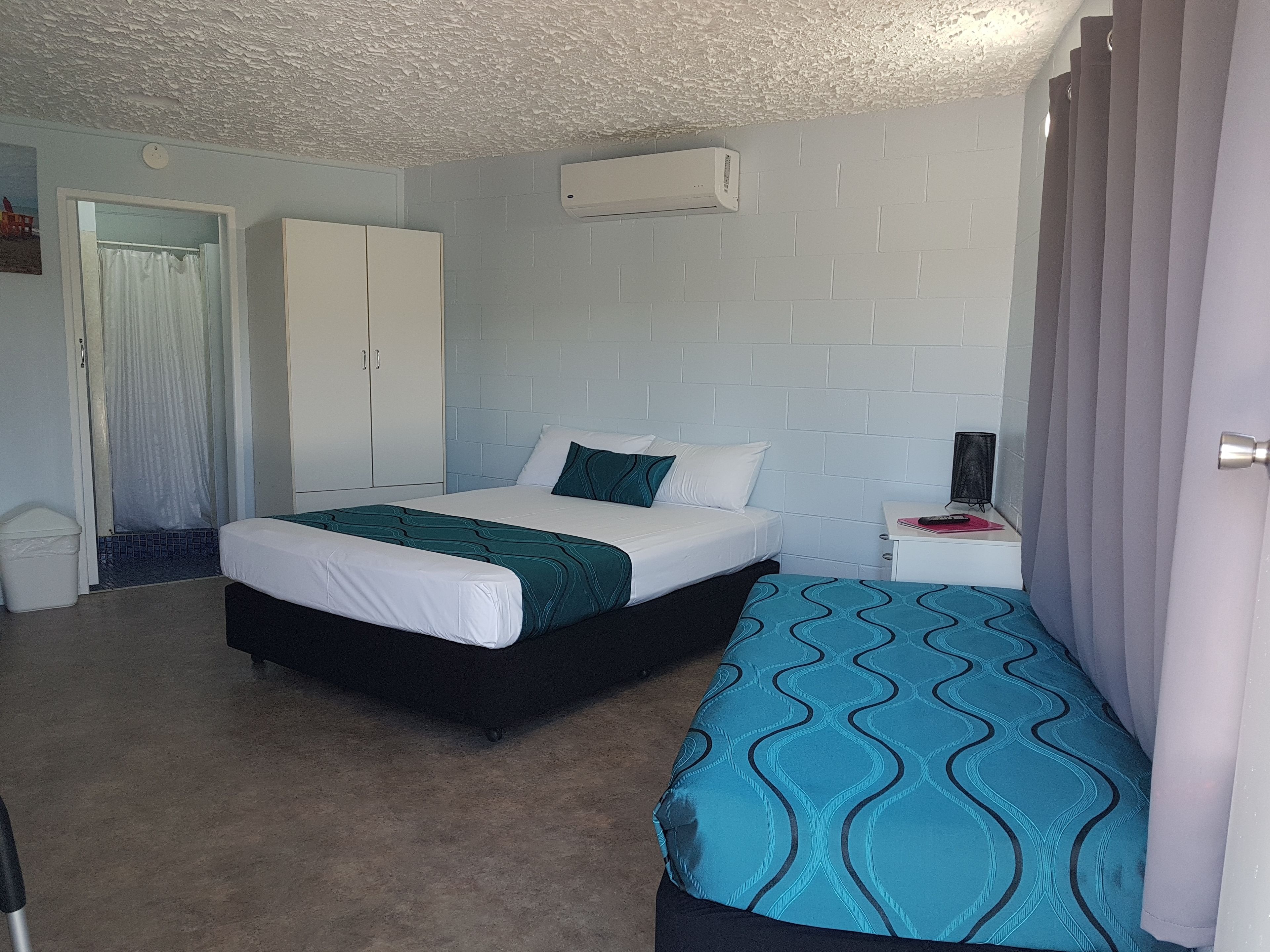 A bedroom with a bed, a nightstand, a wardrobe, and an air conditioning unit.