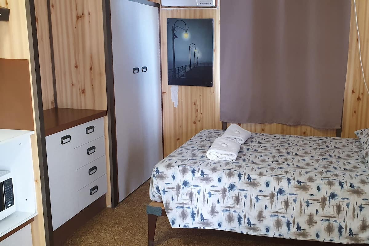 A compact bedroom with a bed, a dresser, a microwave, and a door with a poster.