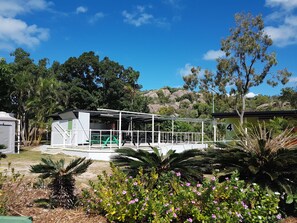 A covered outdoor area with a picnic table, surrounded by lush greenery and a mountain backdrop. - Horseshoe Bay Resort (Bowen)