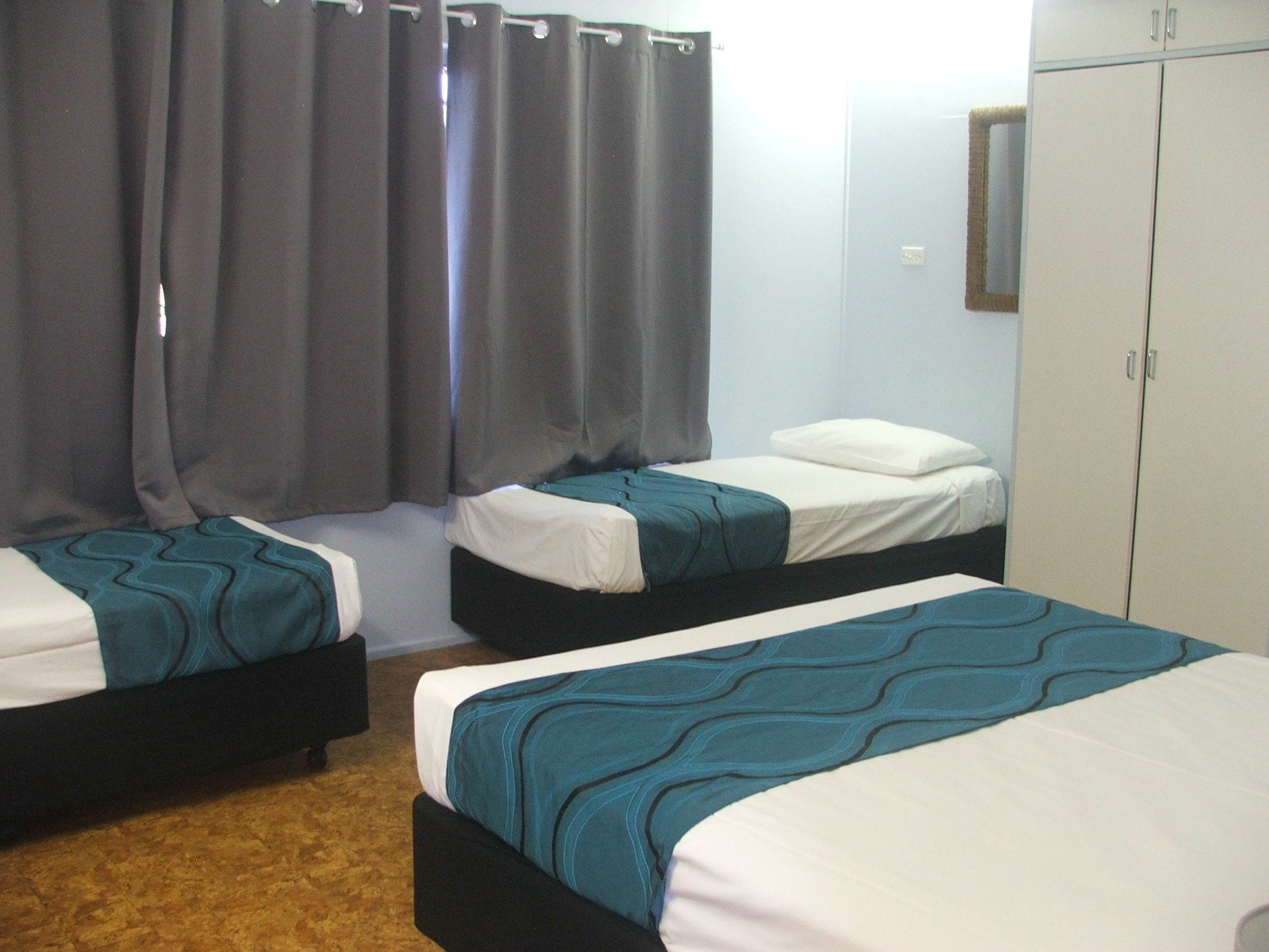 A hotel room with two single beds, a wardrobe, and a mirror on the wall.