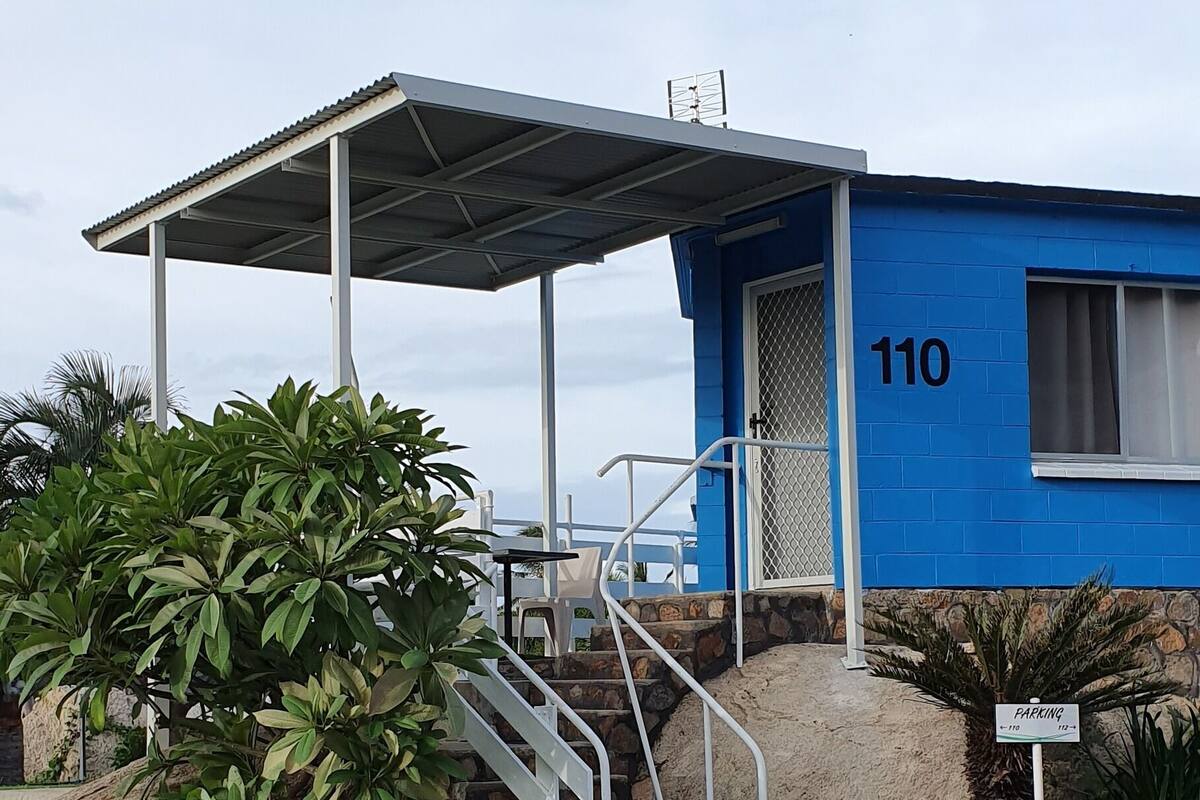 A blue building with the number 110, a covered staircase, and a sign indicating a parking area.