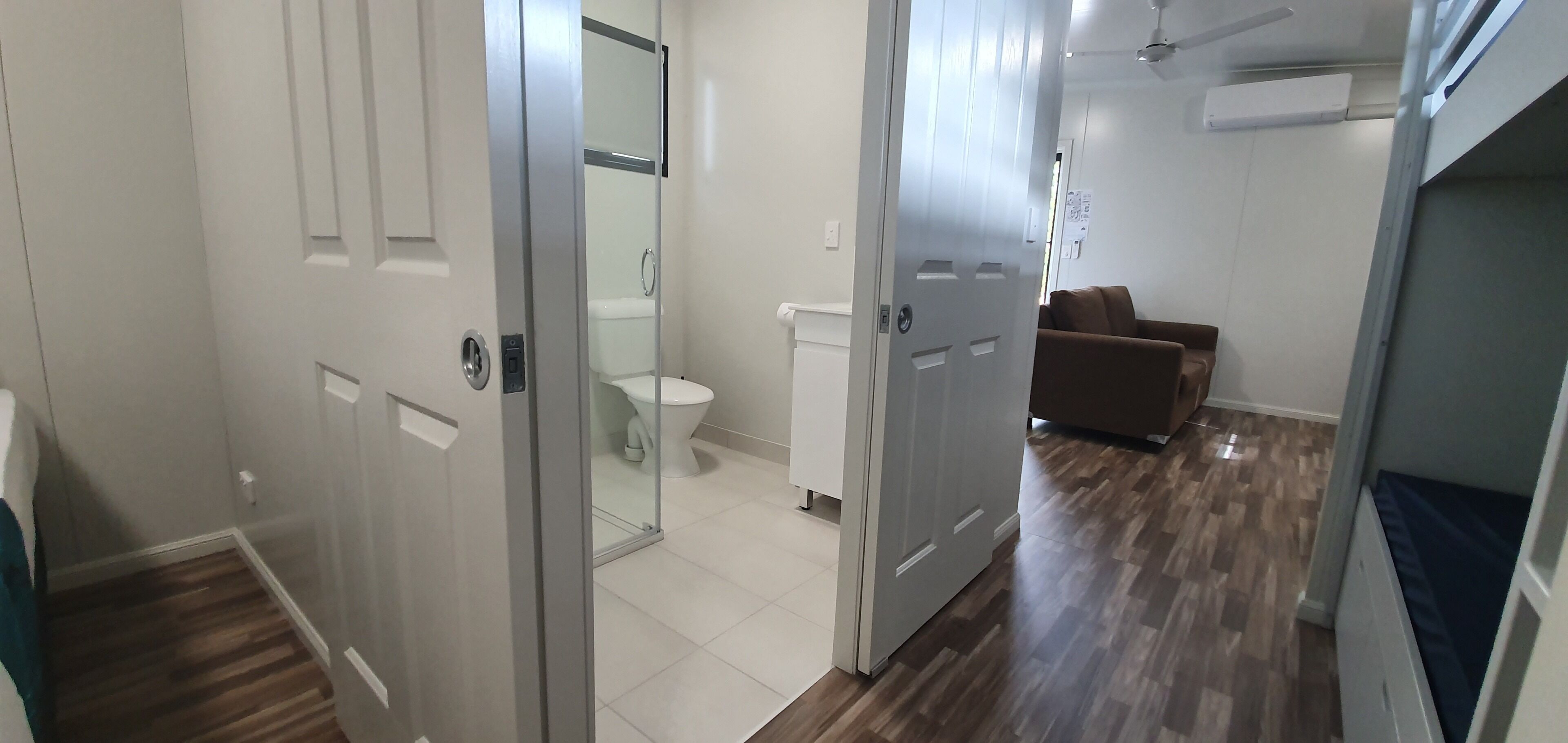 A hallway with a white toilet, a brown sofa, and a ceiling fan.