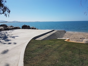 A concrete pathway leading to a beach with a grassy area and a view of the ocean. - Horseshoe Bay Resort (Bowen)
