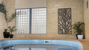 An indoor swimming pool with a clear view of the pool, potted plants, and decorative window panels. - Motel on A'beckett (Inverloch)