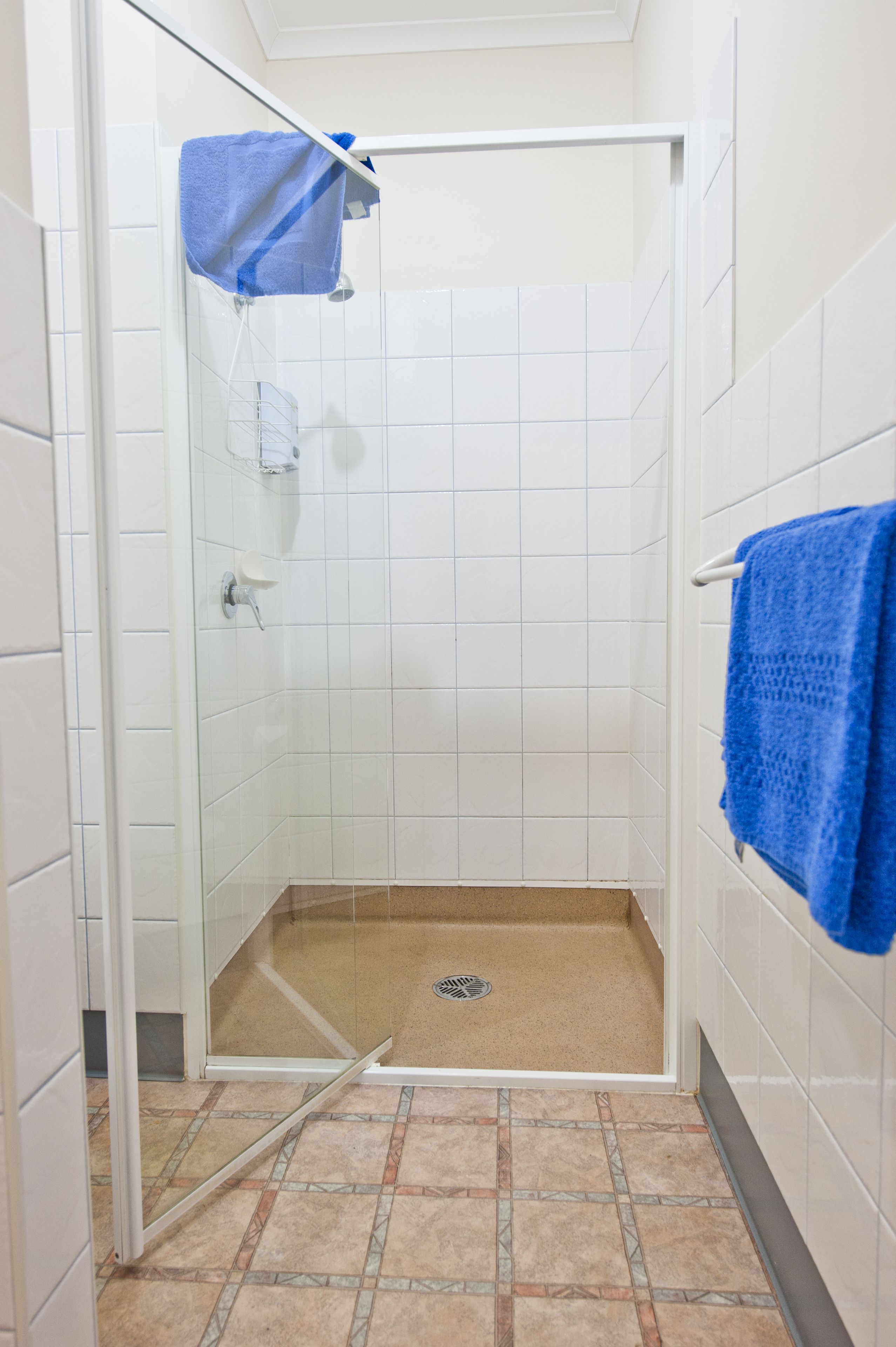 A shower with a glass door, white tiled walls, and a blue towel hanging on the wall.