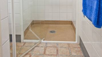 A shower with a glass door, white tiled walls, and a blue towel hanging on the wall.