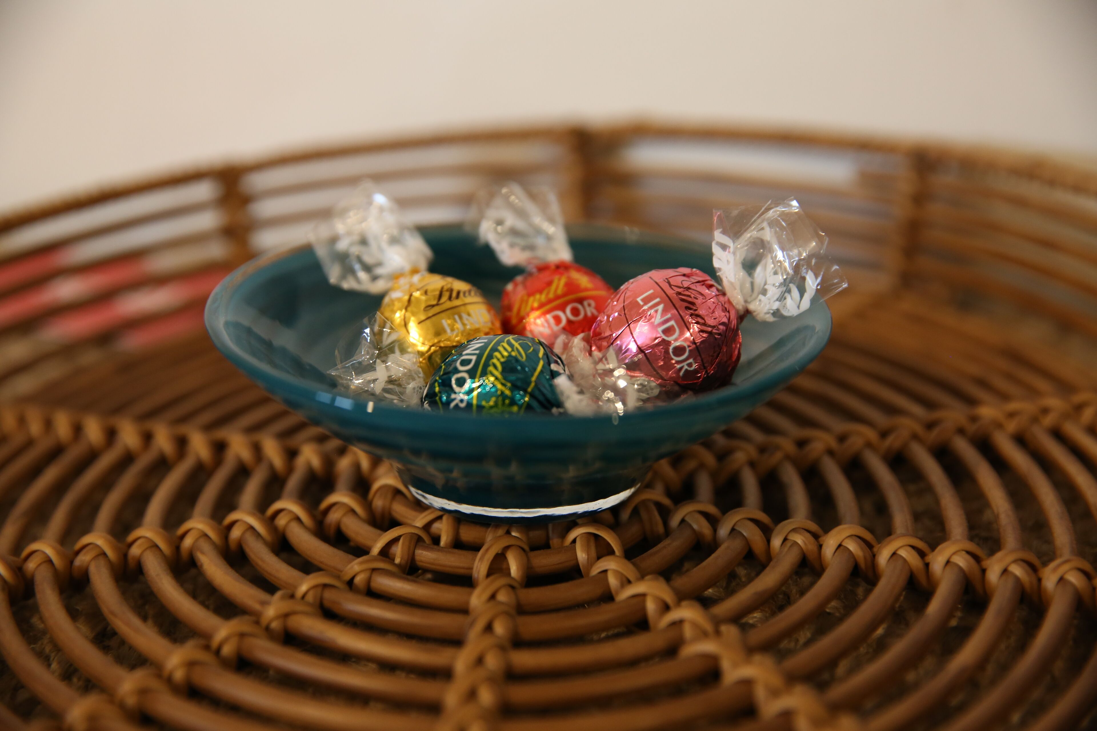 A blue bowl filled with wrapped chocolates on a woven surface.