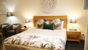 A neatly arranged hotel room with a large bed, two nightstands, a wall-mounted decorative piece, and two chairs. - Motel on A'beckett (Inverloch)