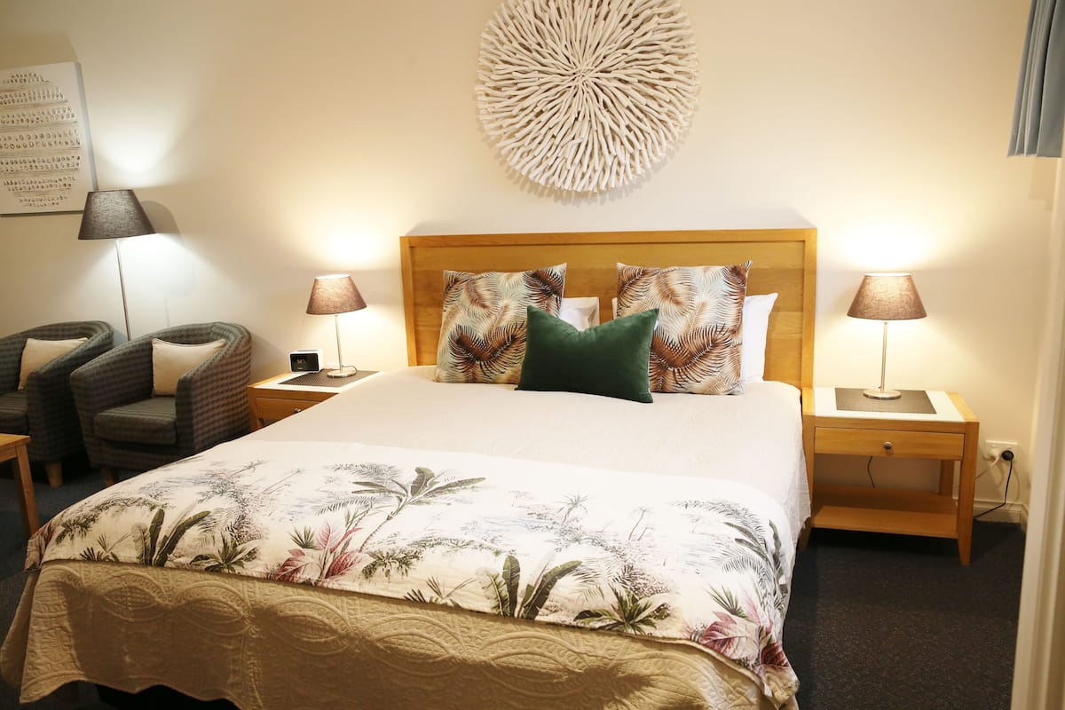 A neatly arranged hotel room with a large bed, two nightstands, a wall-mounted decorative piece, and two chairs.