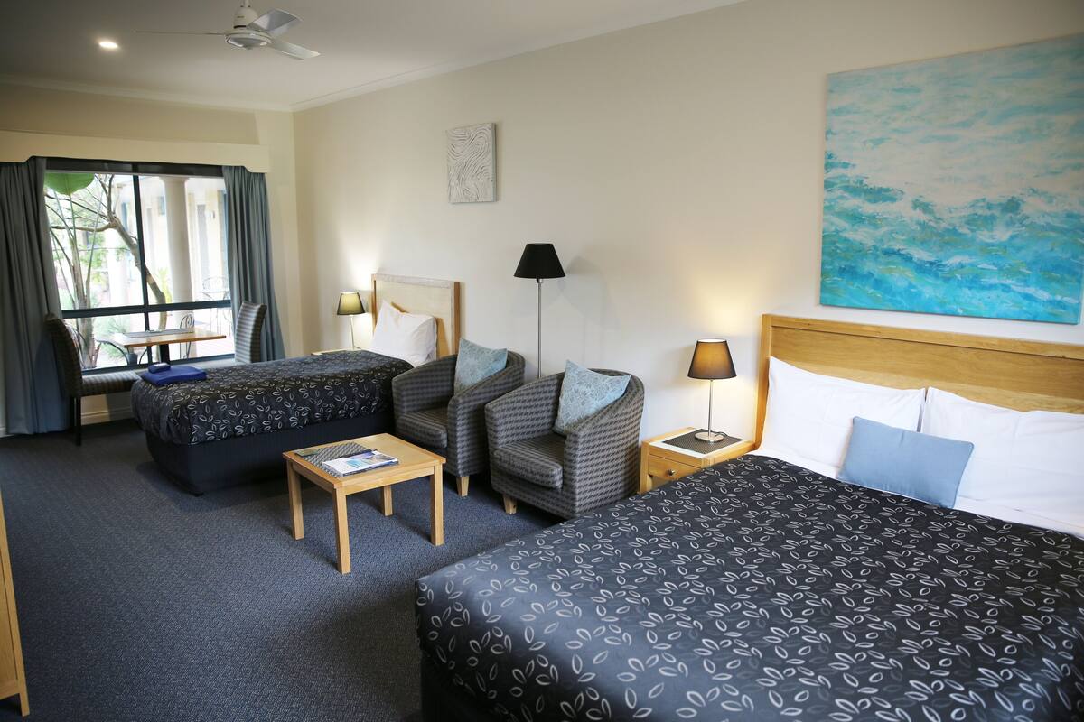A hotel room with two beds, a sofa, a small table, and a window with curtains.