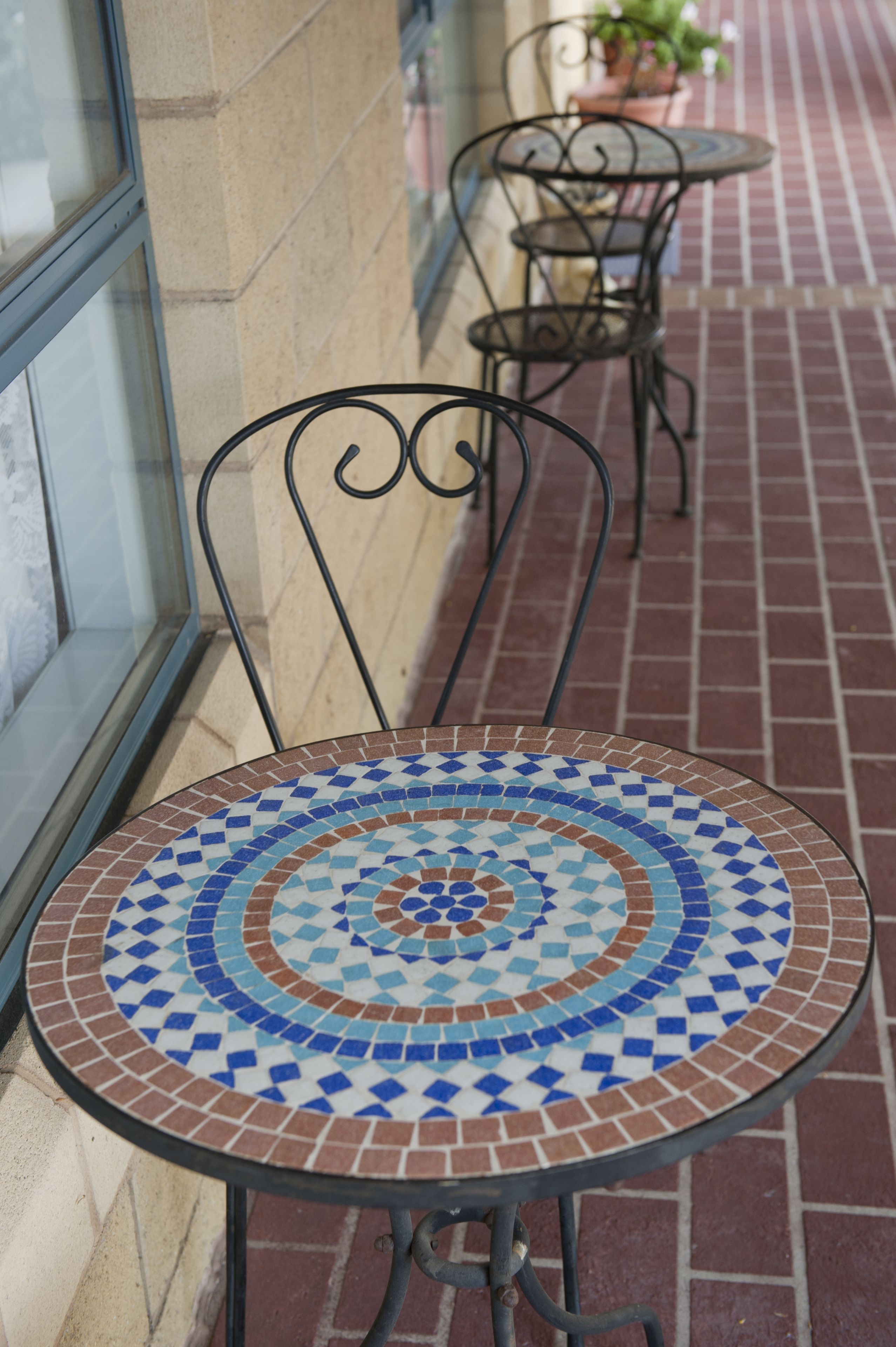 Une table d’extérieur recouverte de carreaux, accompagnée d’une chaise en métal, placée sur un chemin pavé de briques.
