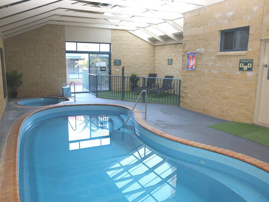 Una piscina interior con solárium de baldosas, un ventanal y una puerta a la derecha.