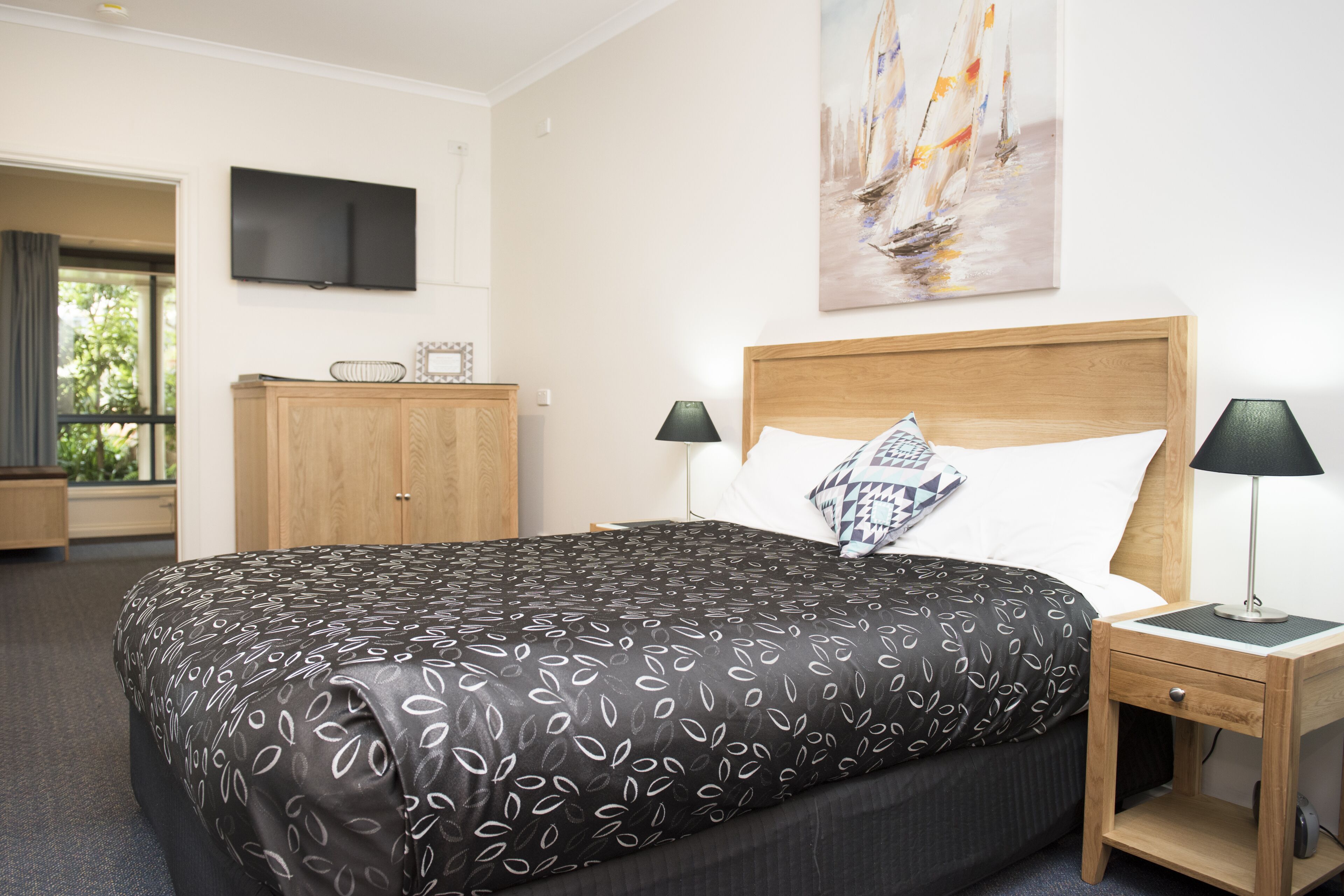 A hotel room with a large bed, two bedside tables with lamps, a flat-screen TV mounted on the wall, and a painting above the bed.