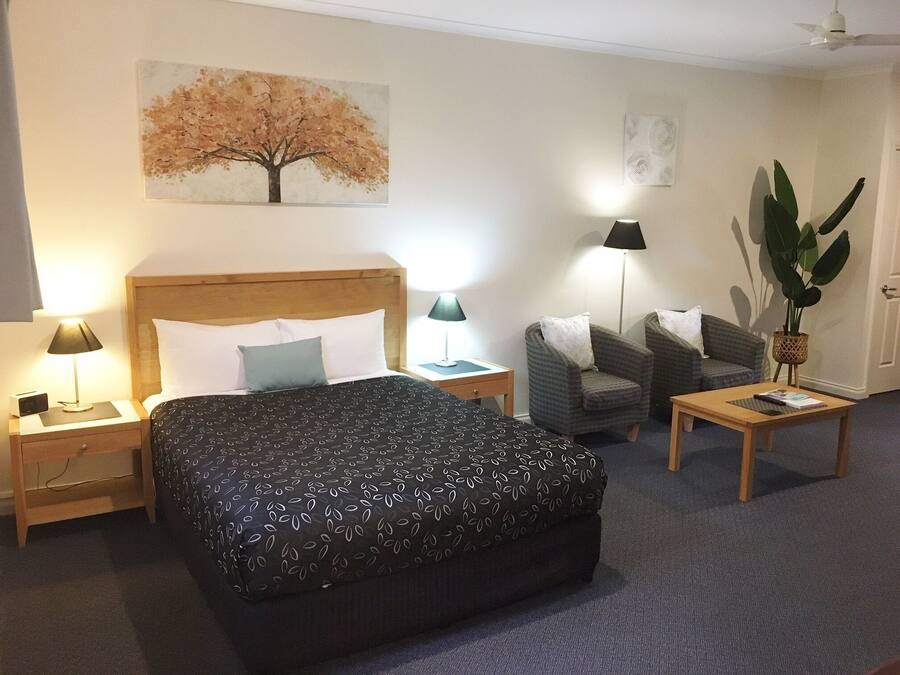 Una habitación de hotel con una cama grande, dos sillones, una mesita, un escritorio y una planta en maceta.