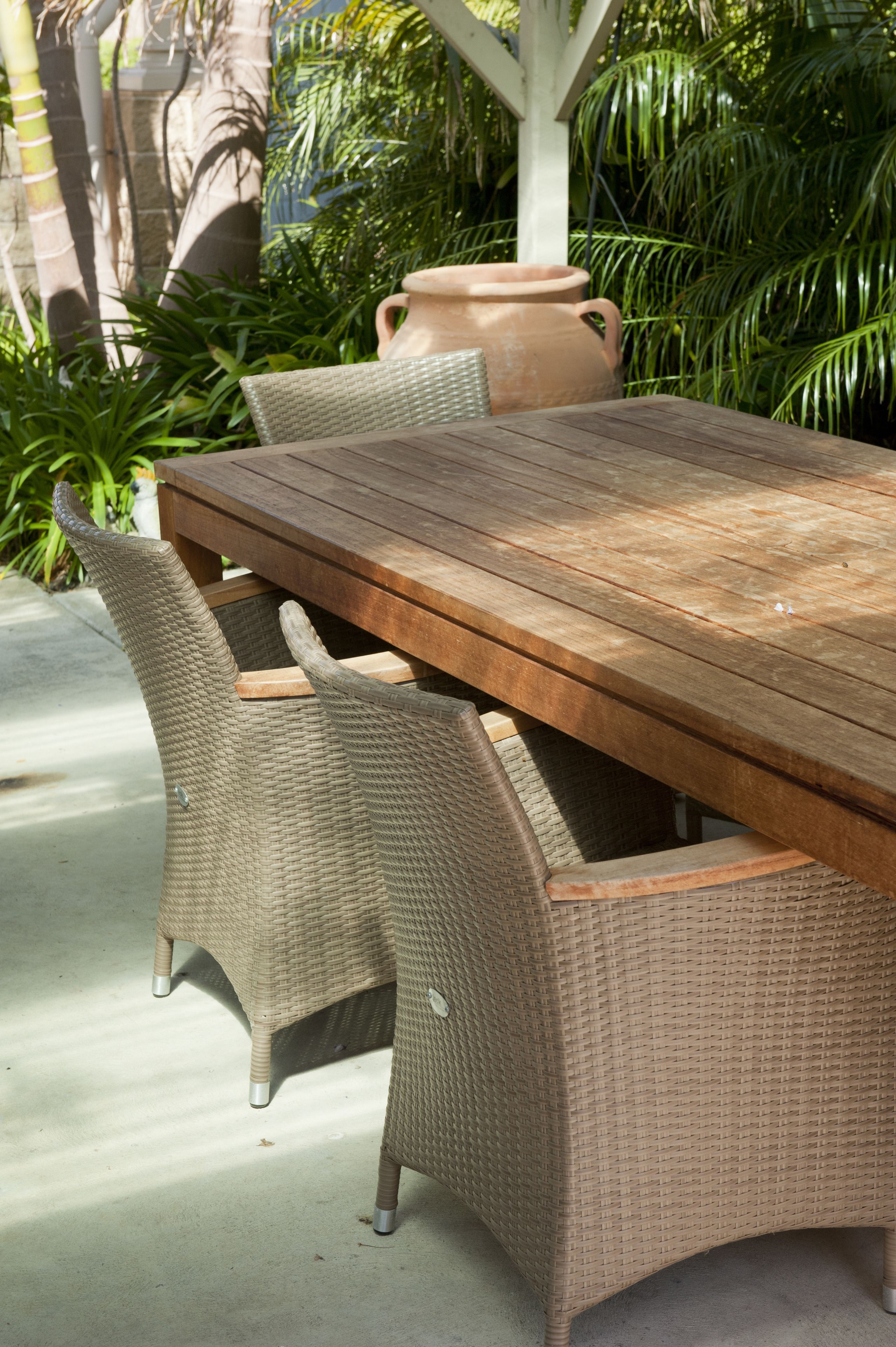 A wooden table with wicker chairs, surrounded by greenery and a stone wall.