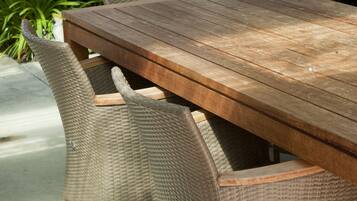 A wooden table with wicker chairs, surrounded by greenery and a stone wall.