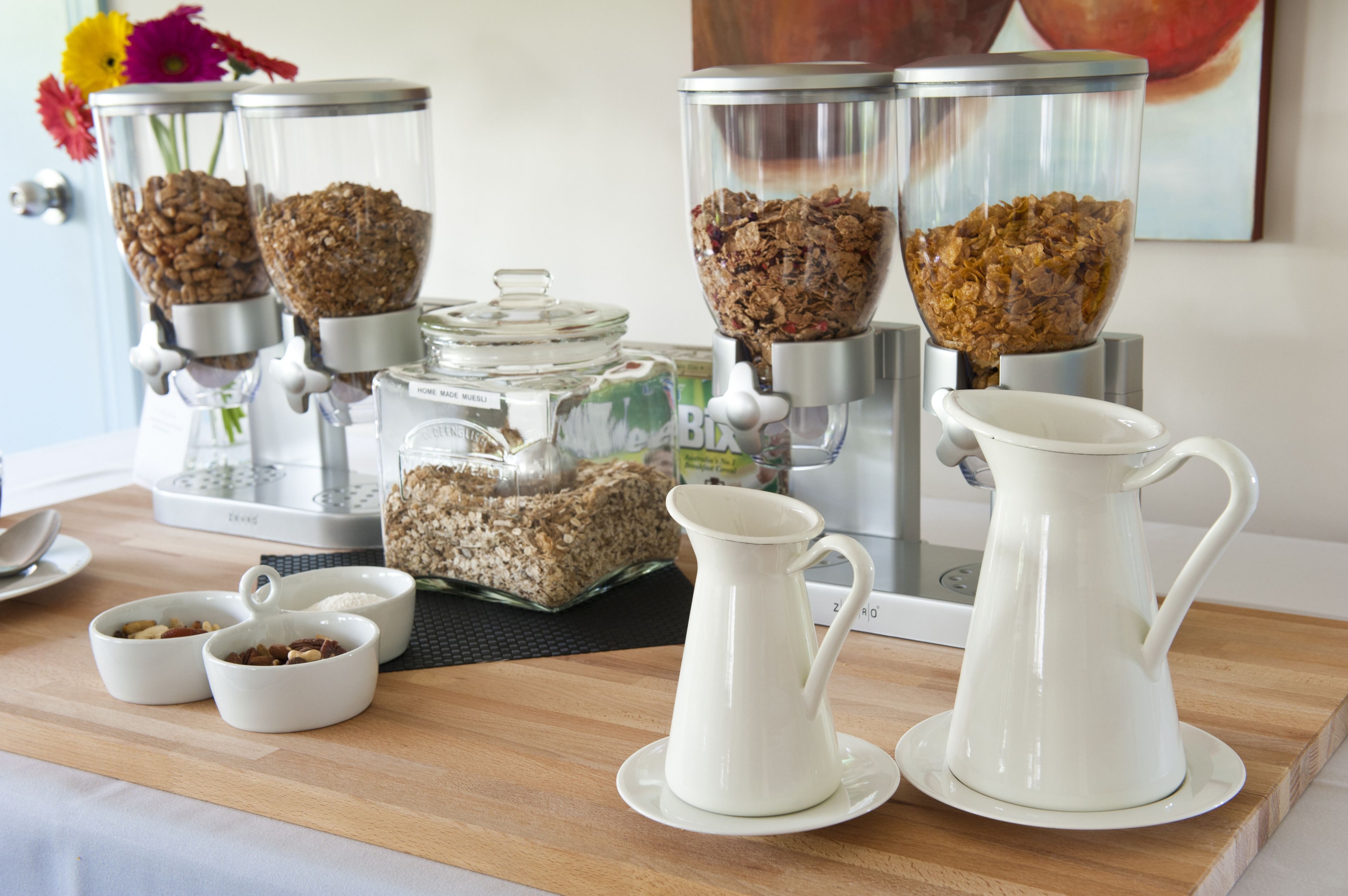 Ein Frühstücksbuffet mit Kaffeemaschine, Getreidespender und zwei Karaffen auf einer Holztischplatte.