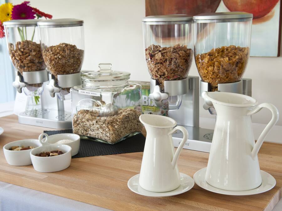 Ein Frühstücksbuffet mit Kaffeemaschine, Getreidespender und zwei Karaffen auf einer Holztischplatte.