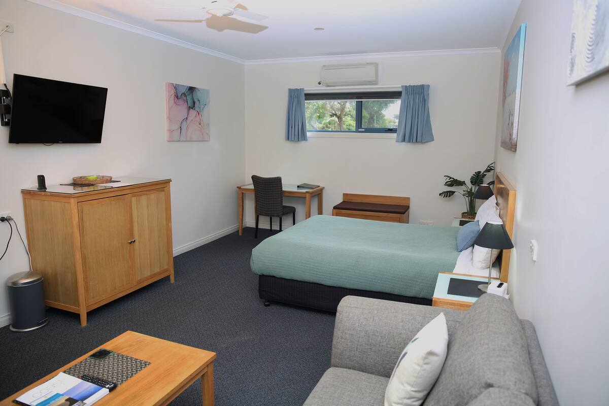 A hotel room with a bed, a desk, a chair, a sofa, a television, and a window with curtains.