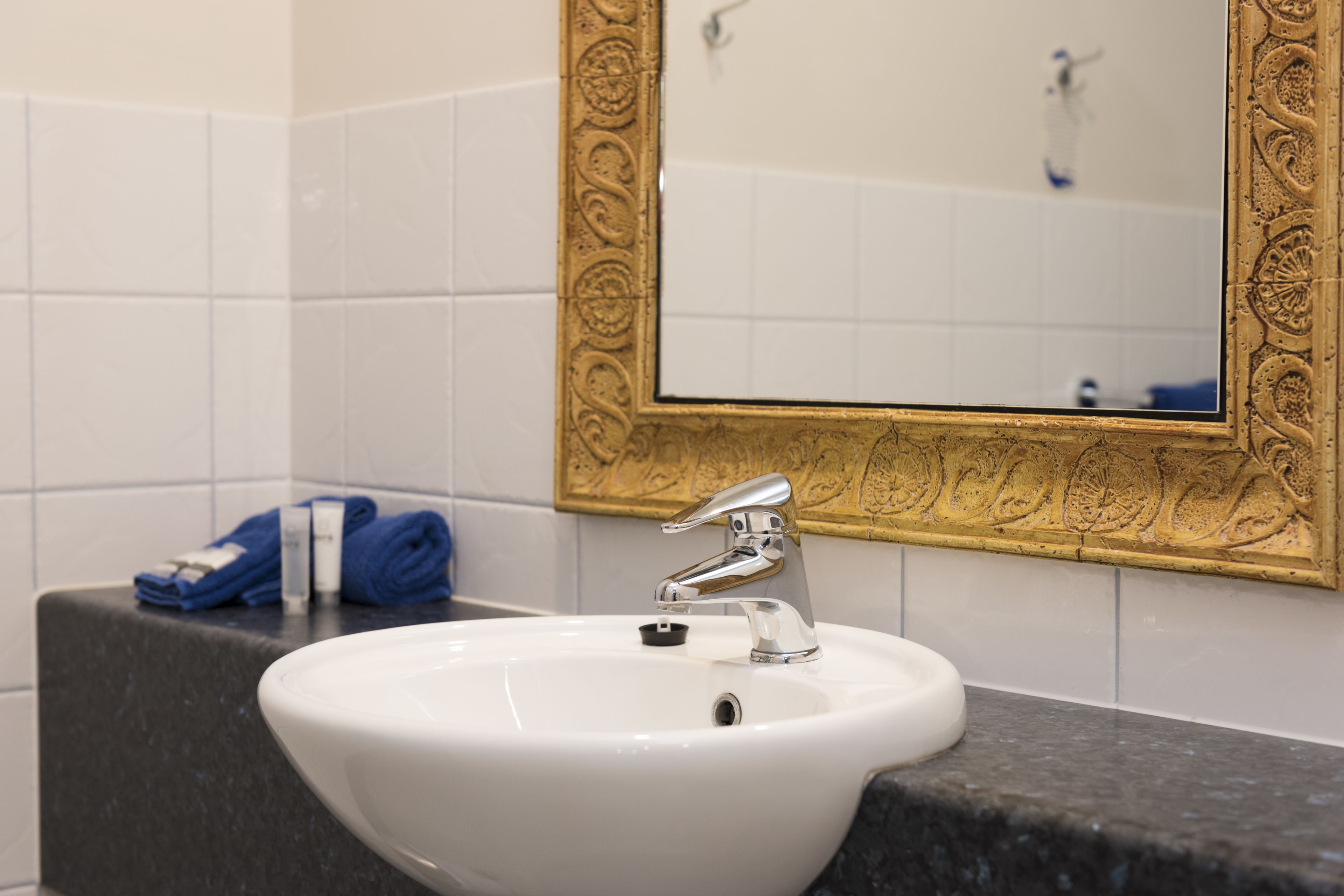 A bathroom with a white sink, a gold-framed mirror, and a black countertop.