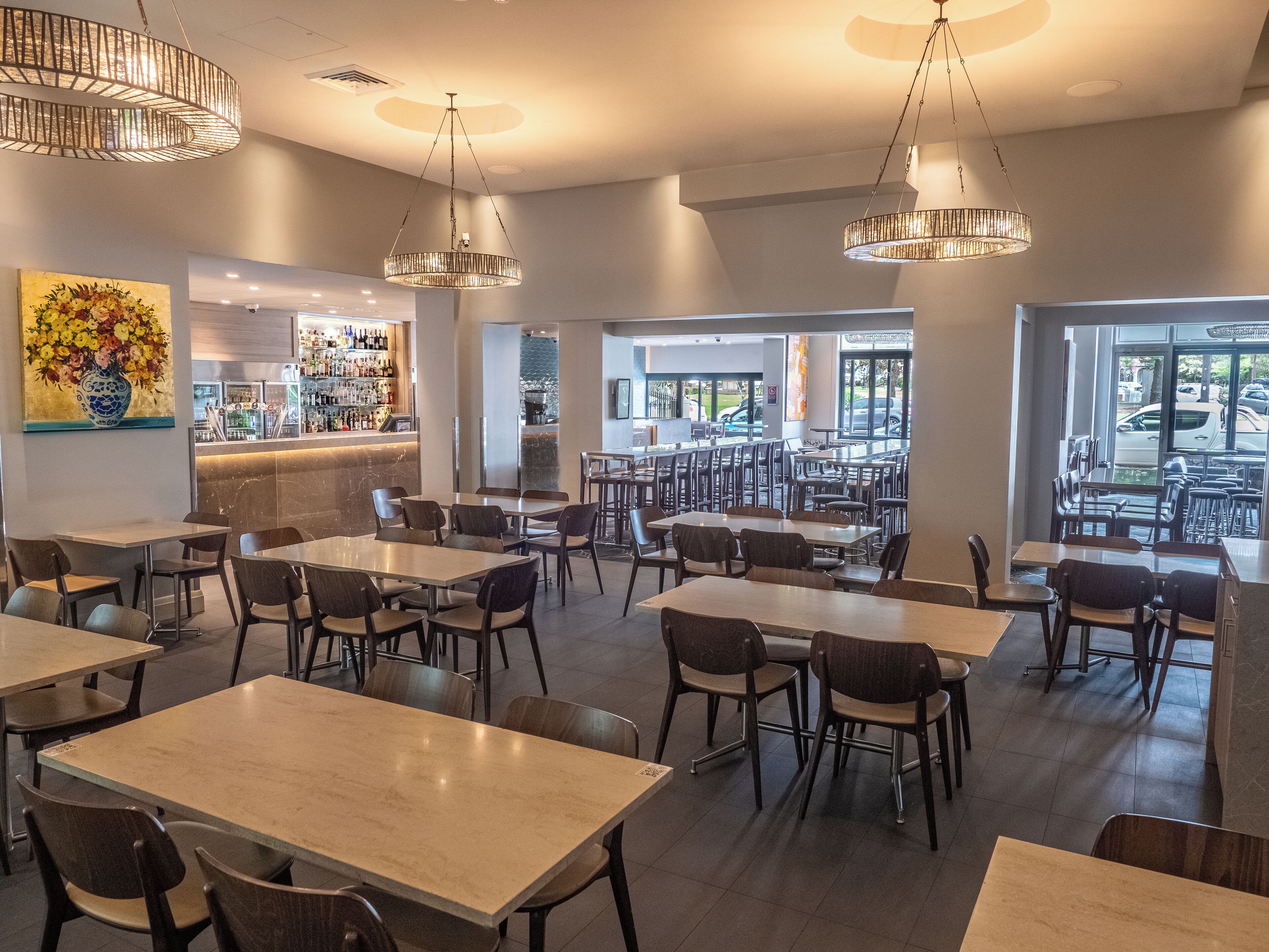 A spacious restaurant with multiple tables and chairs, a bar area, and large windows offering a view of the parking lot.