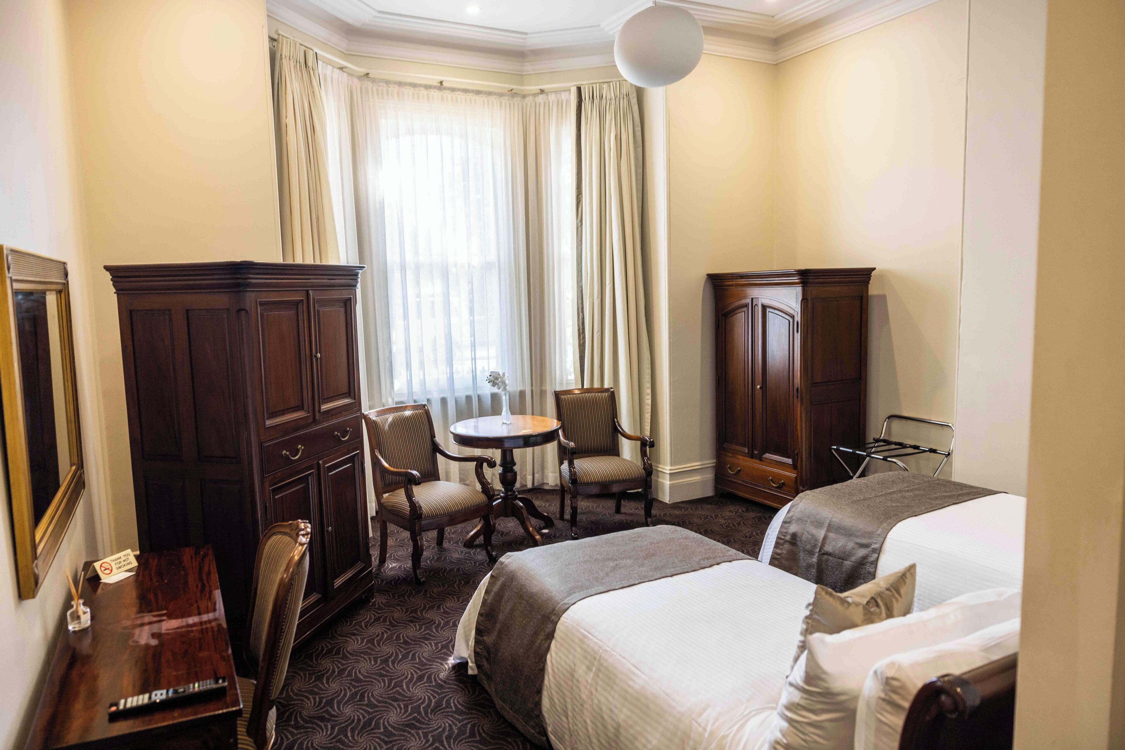 A hotel room with two beds, a desk, a chair, a wardrobe, and a window with curtains.
