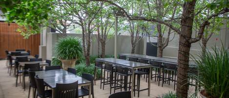 An outdoor patio area with multiple tables and chairs, surrounded by greenery and trees.