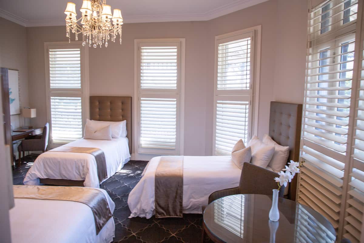 A hotel room with two beds, a desk, a chair, and a chandelier.