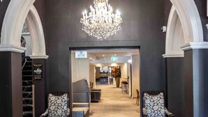 A grand entrance with a chandelier, two patterned armchairs, and a carpeted floor leading to a reception area. - Royal Hotel Randwick (Randwick)