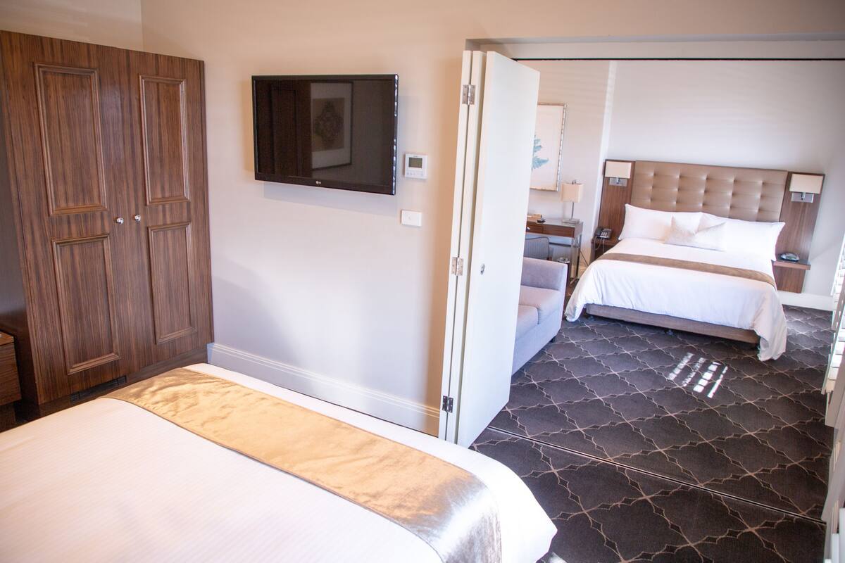 A hotel room with two beds, a TV mounted on the wall, and a separate seating area with a sofa.