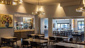 A restaurant with multiple tables and chairs, a bar area with bottles, and a large window providing a view of the street. - Royal Hotel Randwick (Randwick)