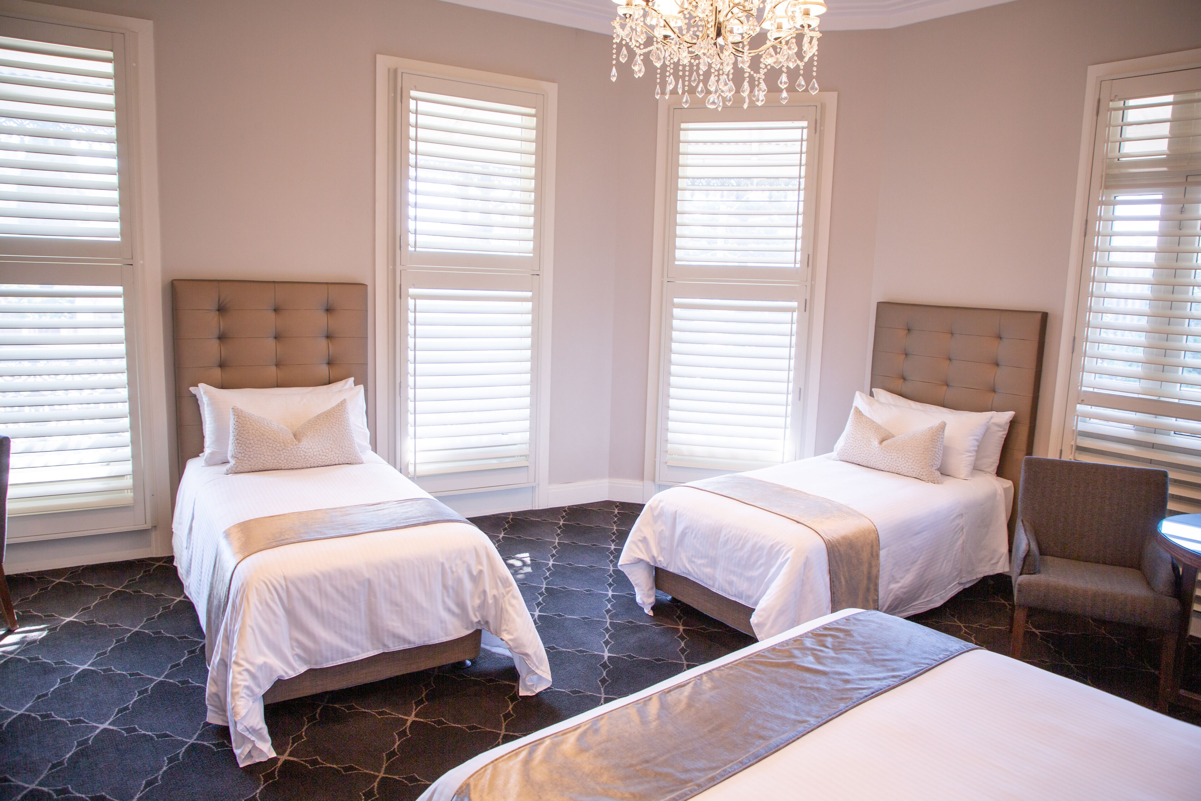 A hotel room with two beds, a chandelier, and large windows with blinds.